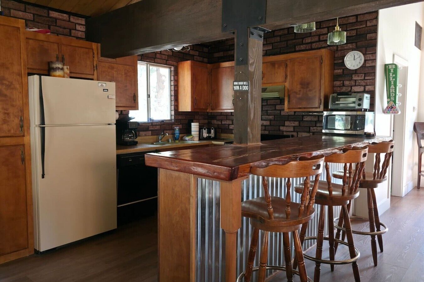 A kitchen with wooden cabinets, a refrigerator, a sink, a microwave, and a bar area with stools.