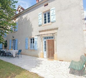 A building with a stone-paved courtyard, outdoor seating, and a door with a patterned curtain. - Gîtes de France® - Chez Madeleine (VARAIRE)