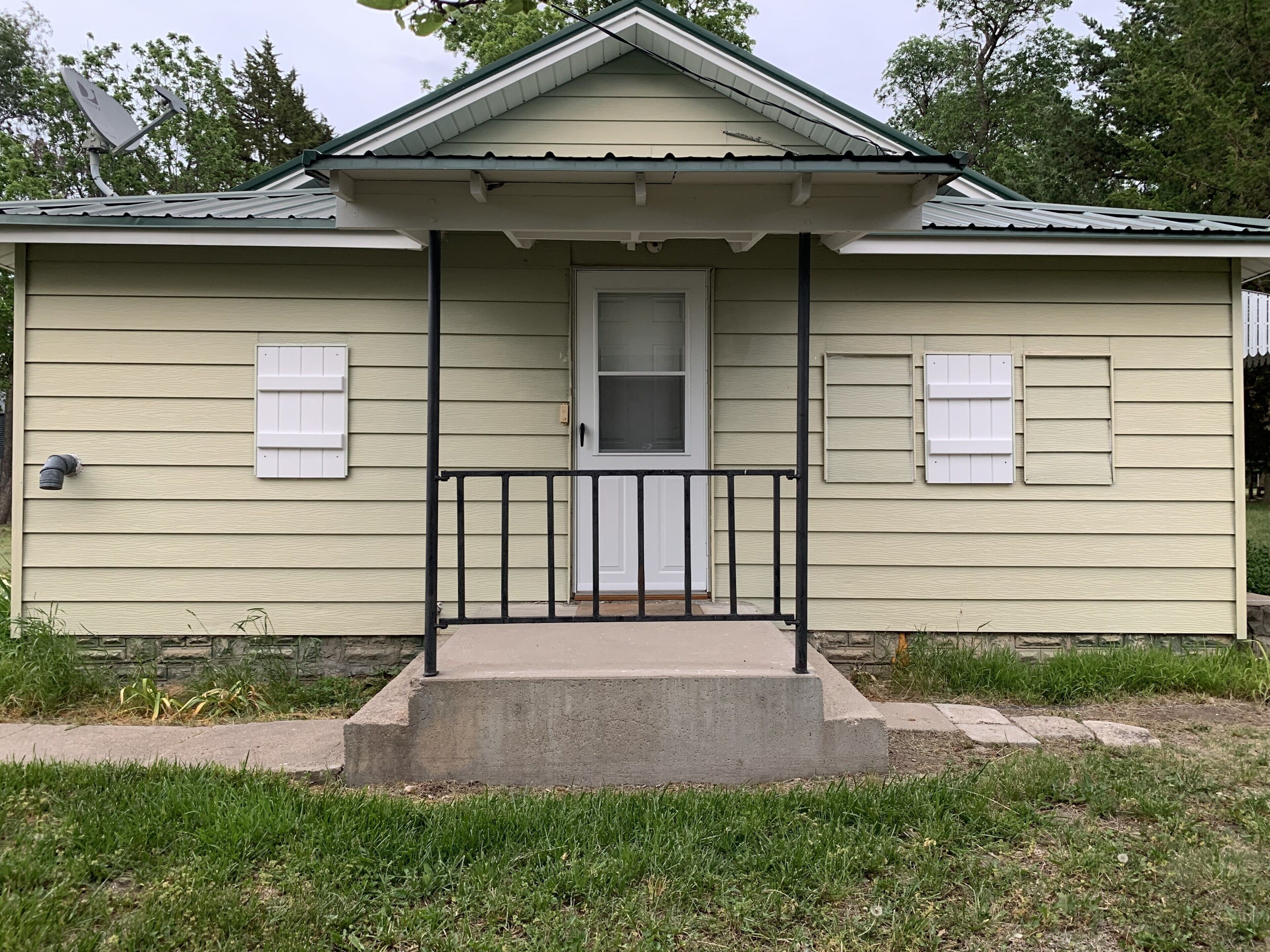 A single-story house with a front porch, a door, and two windows with shutters.