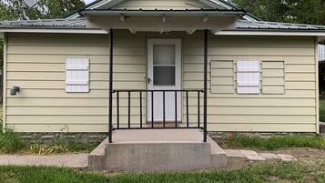 A single-story house with a front porch, a door, and two windows with shutters.
