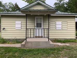 A single-story house with a front porch, a door, and two windows with shutters.