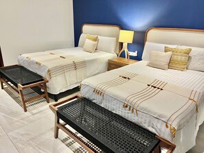 Hotellihuone, jossa on kaksi sänkyä, yöpöytä lampun kanssa ja penkki.