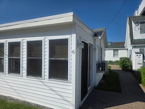A white mobile home with a brick pathway leading to the entrance, a small garden, and a clear blue sky.