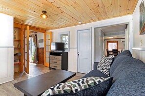 Un salon confortable avec un canapé, une table basse et un téléviseur. Le plafond est en bois et une porte donne accès à une autre pièce.