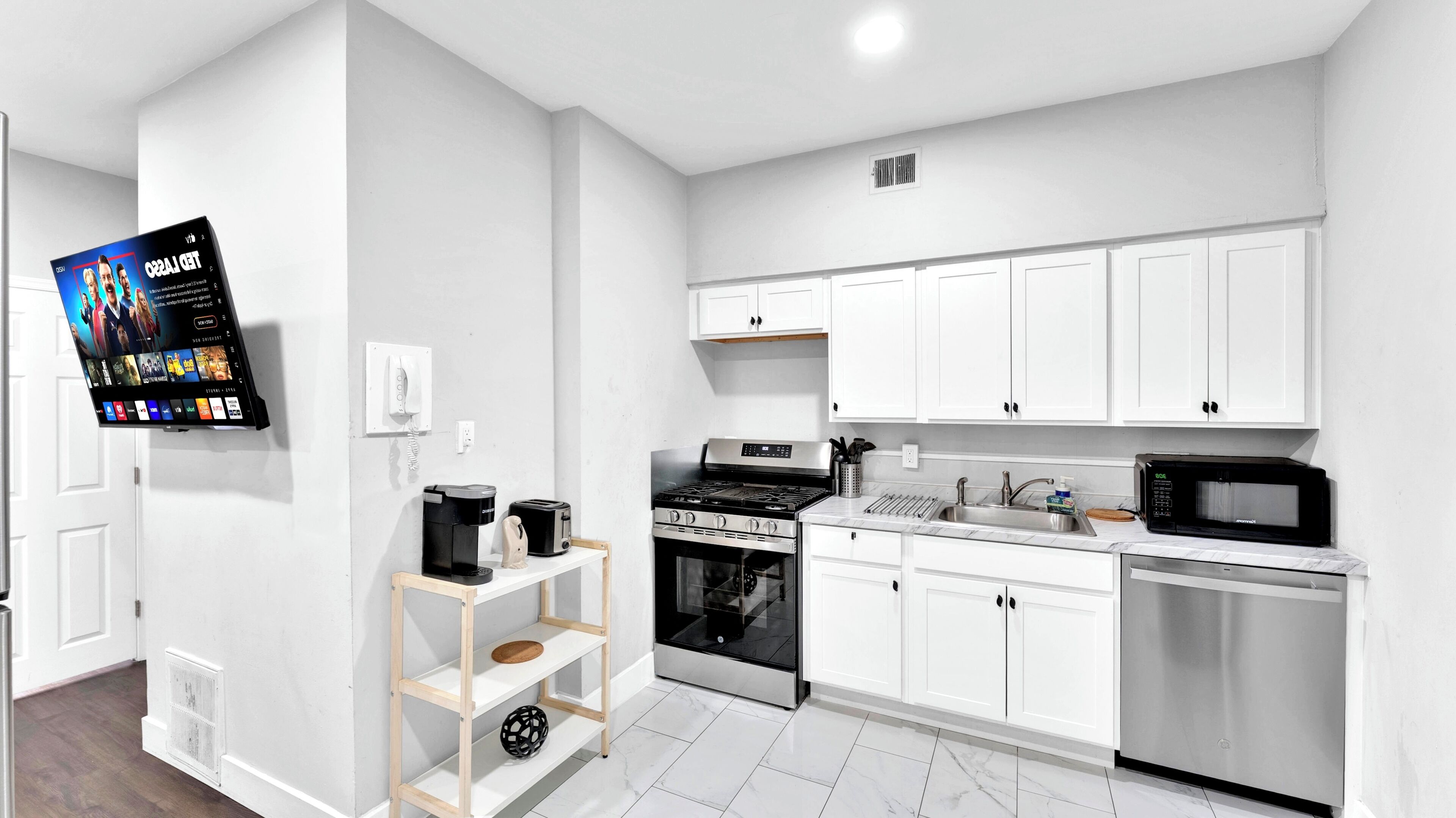 A modern kitchen with white cabinetry, a built-in oven, a microwave, and a coffee maker on a shelf.