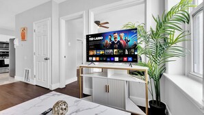 Ein modernes Wohnzimmer mit einem Flachbildfernseher auf einem Standfuß, einem Blumentopf und einem Marmortisch.