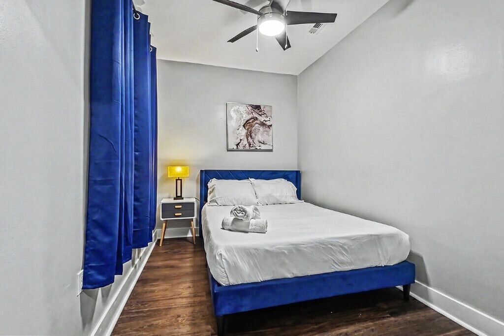 A bedroom with a bed, a ceiling fan, a nightstand, a lamp, and a painting on the wall.