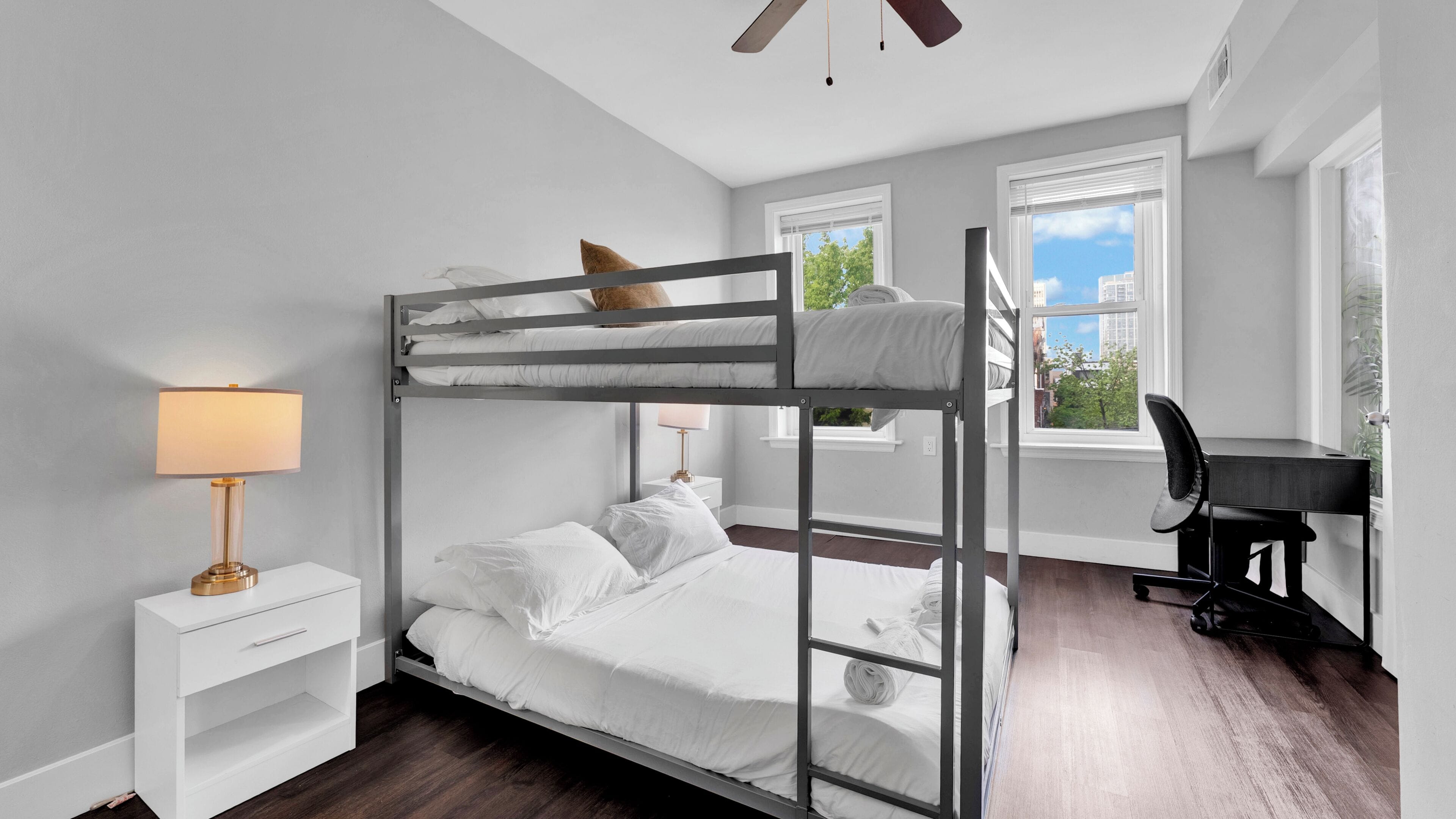 Habitación con literas, escritorio, silla, lámpara y ventanas.