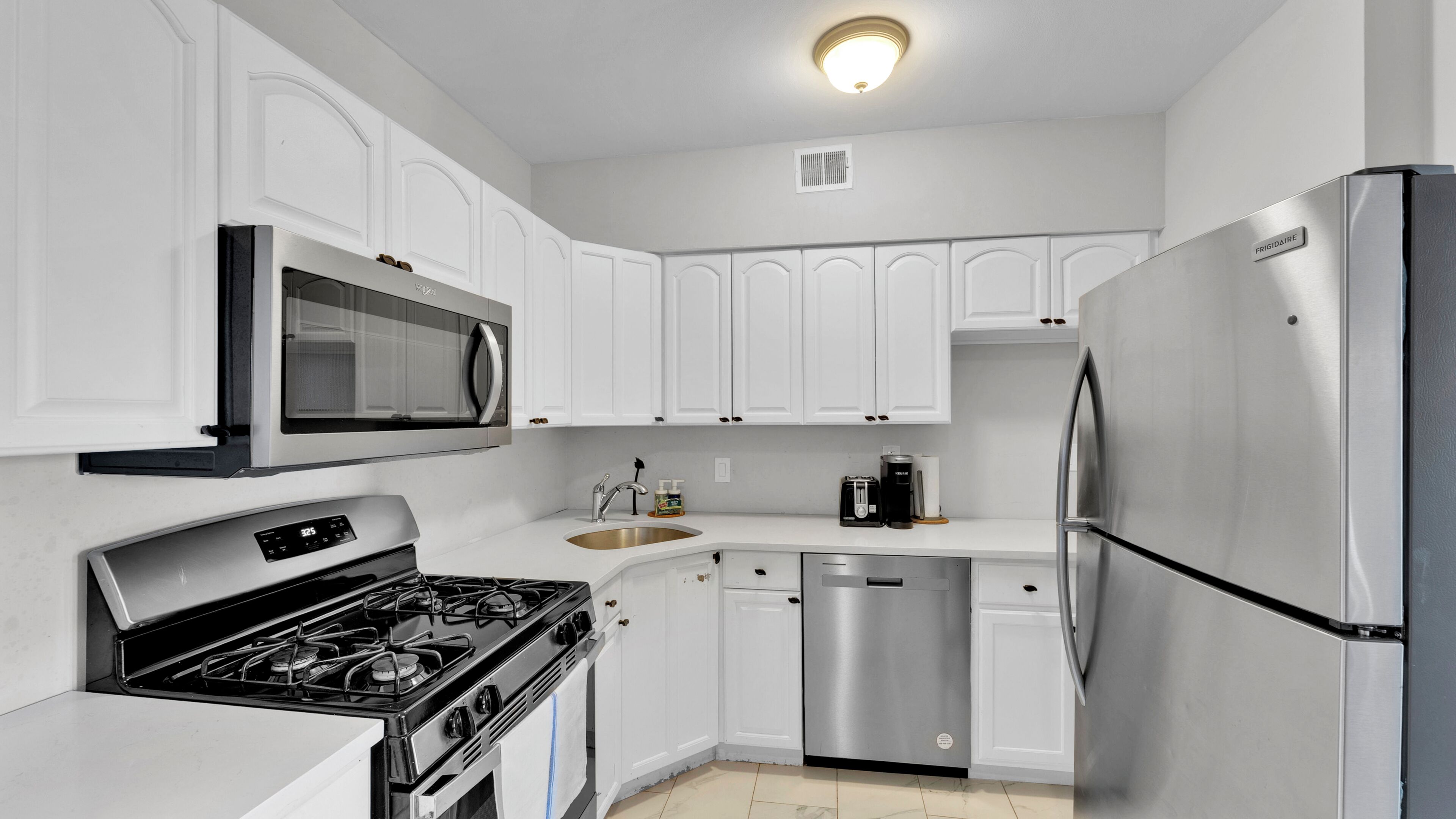 A modern kitchen with white cabinetry, a stainless steel refrigerator, a microwave, a stove, and a dishwasher.