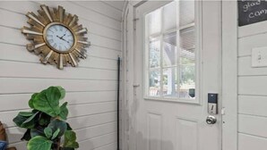 A room with a wall-mounted clock, a potted plant, a broom, and a door with a window.