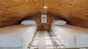 A small, wooden attic room with two beds, a patterned rug, and a framed picture on the wall.