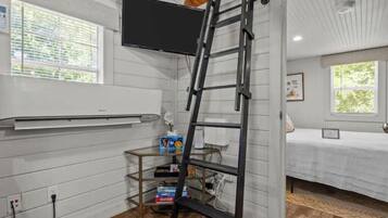 A room with a bed, a TV mounted on the wall, a ladder, and a shelf with items.