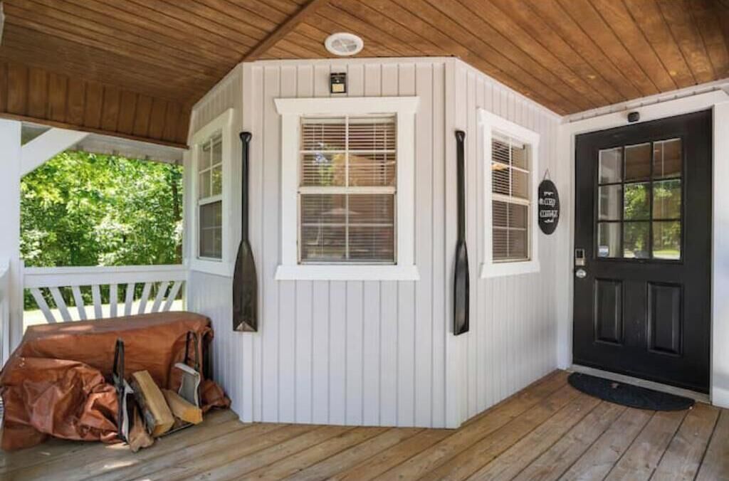 A covered porch with a bench, a black door, and a window with blinds.