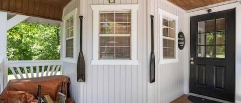 A covered porch with a bench, a black door, and a window with blinds.