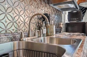 A kitchen with a stainless steel sink, a microwave, and a patterned backsplash.
