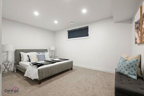 Ein Schlafzimmer mit einem Bett, Nachttischen, einem Fenster und einem Sofa.