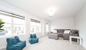 Ein großzügiges Wohnzimmer mit grauem Ecksofa, hängenden Sitzsäcken in Türkis und einem weißen Couchtisch.