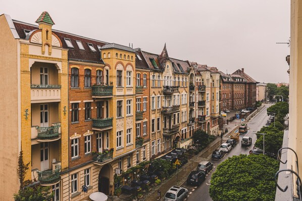 A row of multi-story buildings with balconies, a street with parked cars, and a clear sky.
