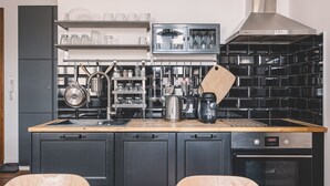 Ett modernt kök med svarta skåp, en bänkskiva i trä, en inbyggd ugn och en kaffemaskin.
