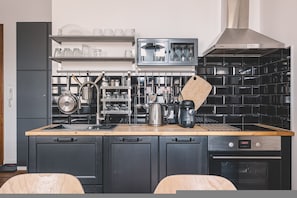 A modern kitchen with black cabinets, a wooden countertop, a built-in oven, and a coffee machine. - Diente Studio Pozna Je yce Balkon Kamienica (gmina Parzęczew)