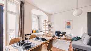 Ett modernt vardagsrum med en matplats, en soffa, en bärbar dator på ett sidobord och ett träställ med upphängda föremål.