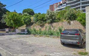 A parking area with a gravel surface, a parked car, and a stone wall with vegetation. - 1 bedroom awesome apartment in Bastia (Bastia)