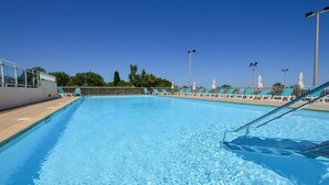 Ein Schwimmbecken mit klarem, blauem Wasser, umgeben von Liegestühlen und Sonnenschirmen, mit blauem Himmel darüber.