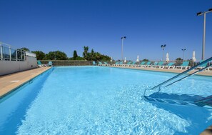 Ein Schwimmbecken mit klarem, blauem Wasser, umgeben von Liegestühlen und Sonnenschirmen, mit blauem Himmel darüber.