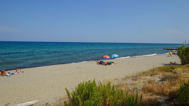 Ein Strand mit blauem Himmel, ruhiger See und badenden Menschen.