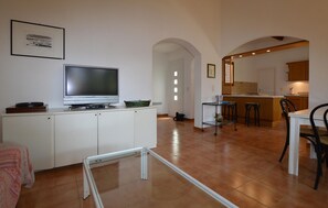 Eine moderne Küche mit Fernseher, ein Essbereich mit Stühlen und einem offenen Durchgang zu einem anderen Raum.
