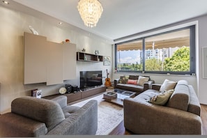 Ein modernes Wohnzimmer mit Flachbildfernseher, einer Gitarre und einem großen Fenster mit Blick auf die Stadt.