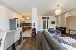 Ein modernes Wohnzimmer mit Sofa, Esstisch, Stühlen, einer Küchenzeile inklusive Schränken und Geräten sowie einem Kronleuchter.