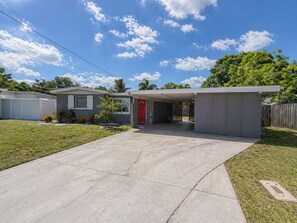 A single-story house with a garage, a red door, and a covered driveway. - 3BR Largo Home Near Indian Rocks & Madeira Beach (Largo)
