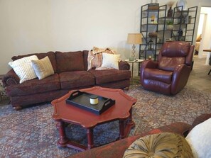 A living room with a brown leather sofa, a brown leather armchair, a small round coffee table, and a patterned rug.