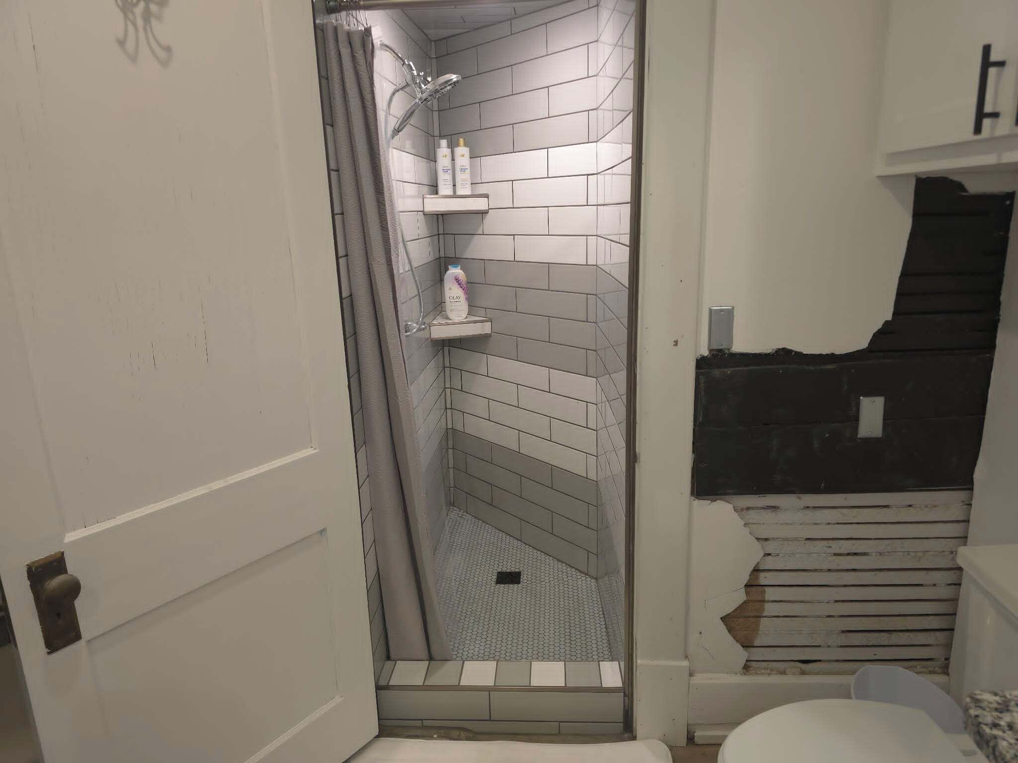 A bathroom with a shower, tiled walls, a toilet, and a shelf with toiletries.