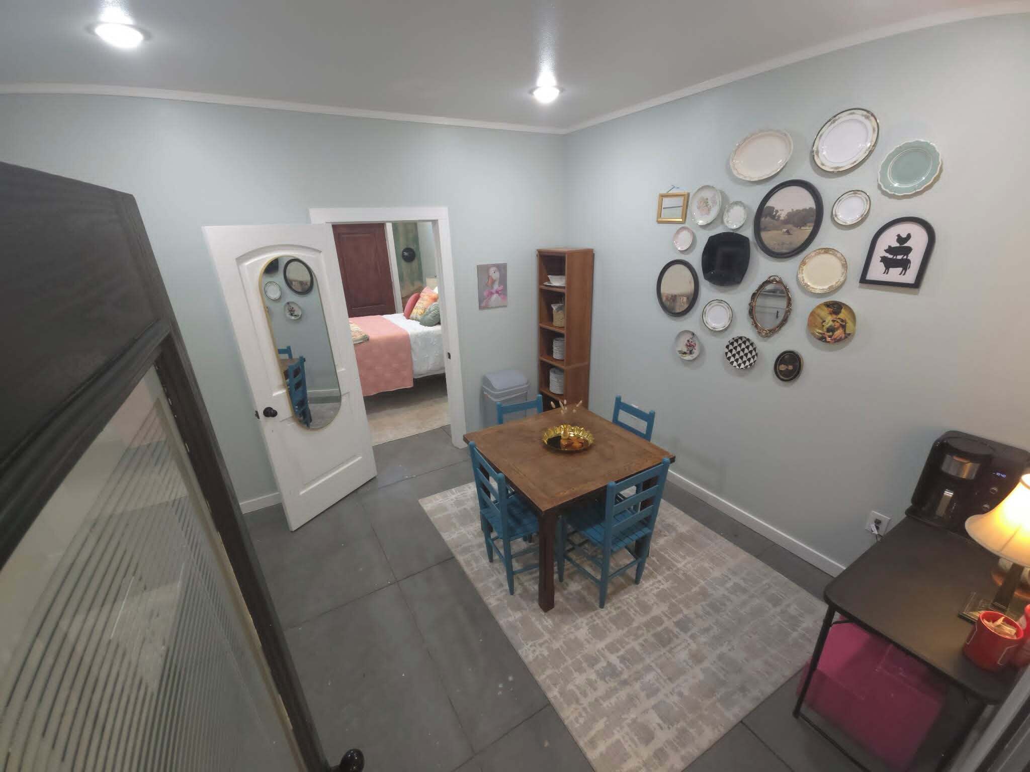 Un comedor con una mesa y sillas de madera, una estantería y una pared decorada con platos y espejos.