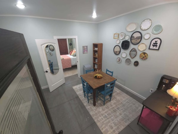 A dining area with a wooden table and chairs, a bookshelf, and a wall decorated with plates and mirrors.