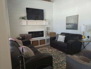 A living room with a flat-screen TV, fireplace, leather sofas, and a patterned rug.