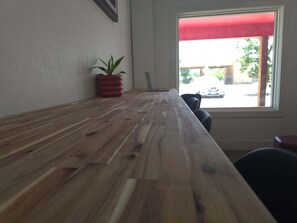 Um balcão de madeira com um vaso de planta, uma janela com toldo vermelho e vista para o exterior.