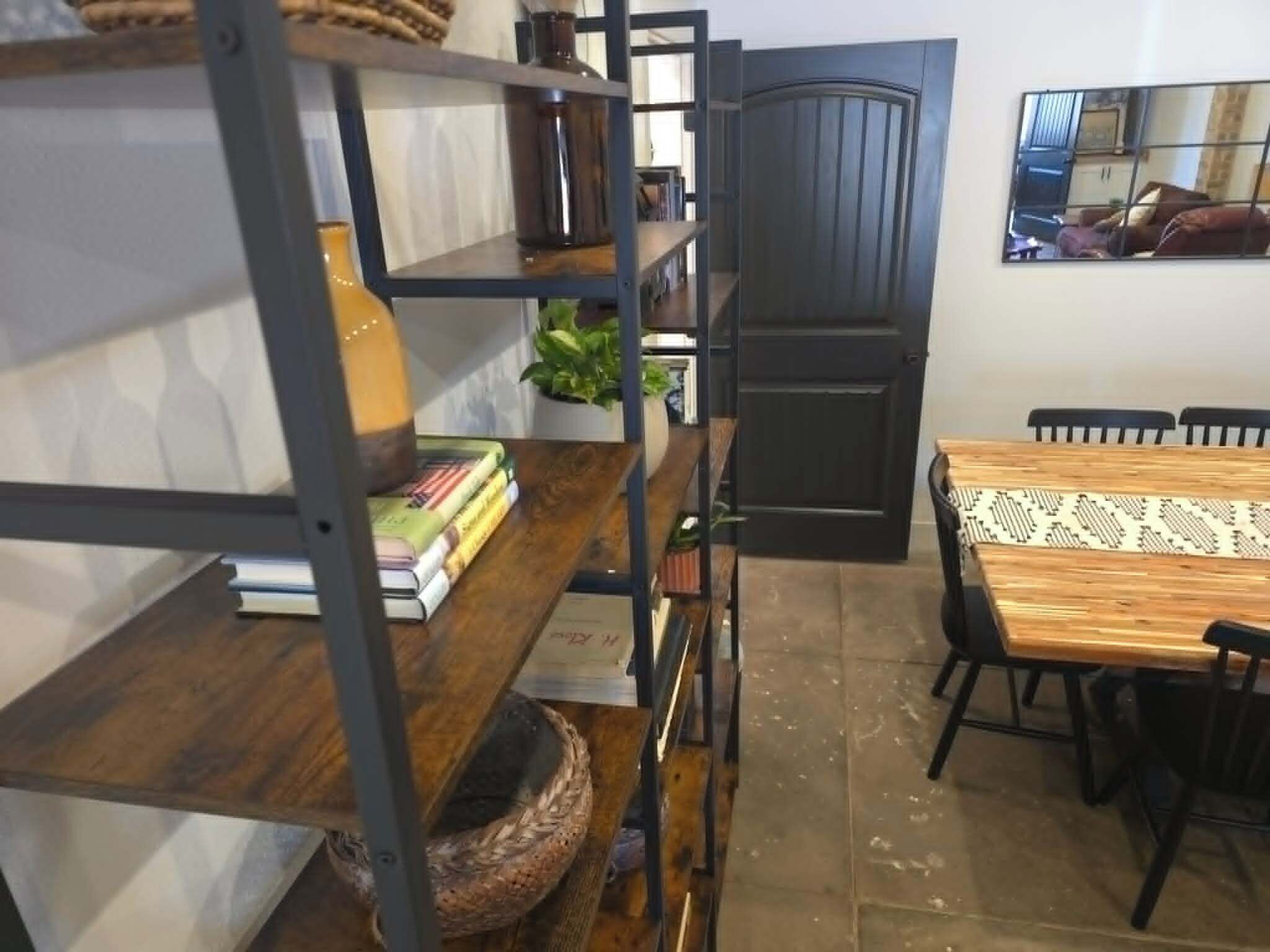 Una habitación con una mesa de madera, sillas, una estantería, una planta en maceta y una puerta.