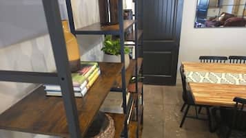 Una habitación con una mesa de madera, sillas, una estantería, una planta en maceta y una puerta.