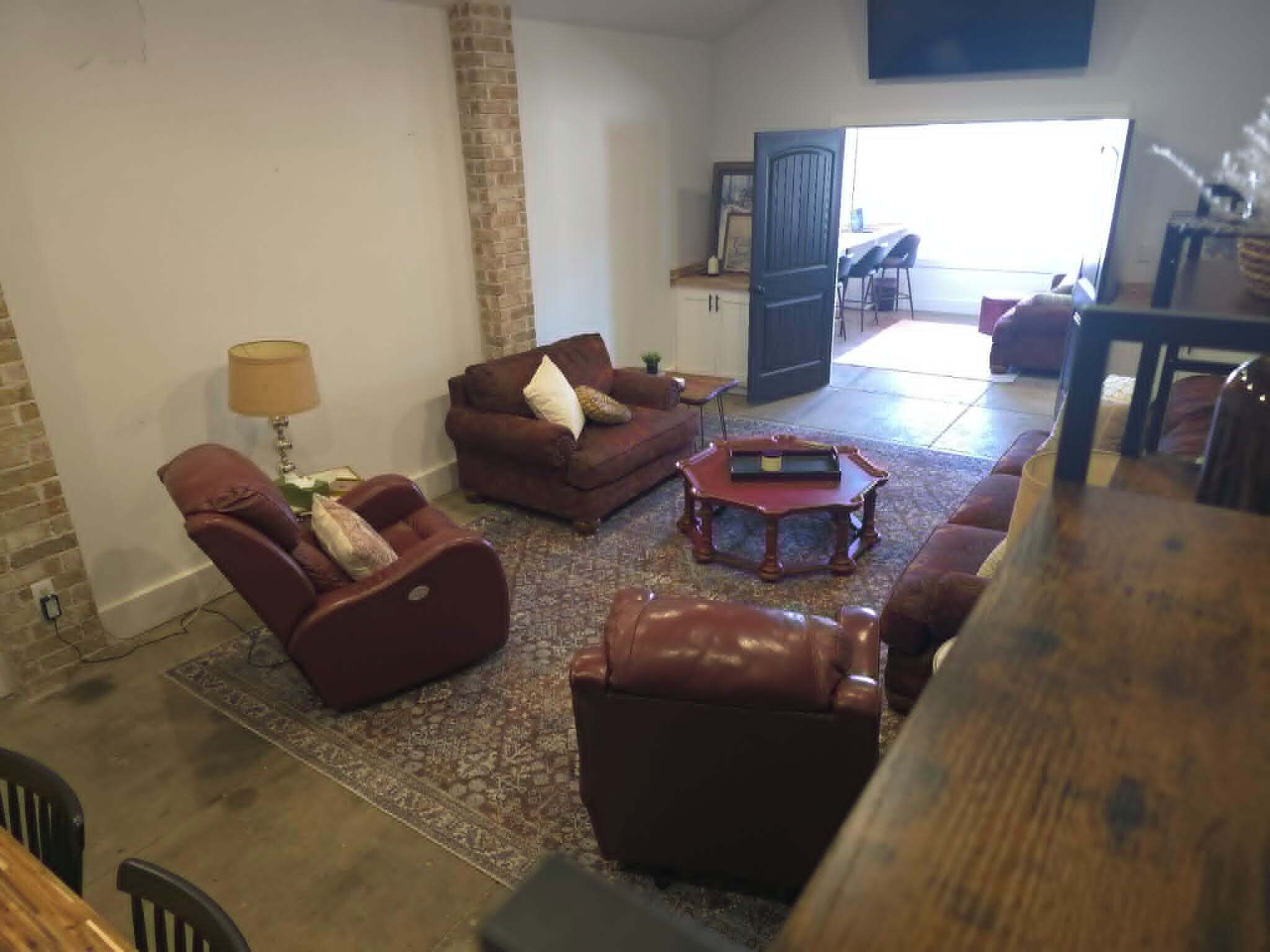 A living room with a sofa, armchair, and coffee table. There is a door leading to another room.