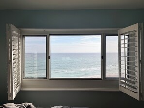 Ein Zimmer mit großem Fenster und Meerblick, einem Bett und einer Wand mit strukturierter Oberfläche.