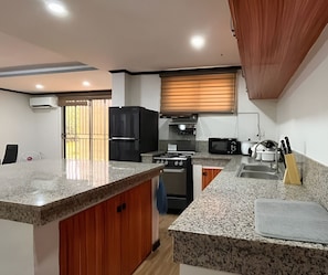 A modern kitchen with granite countertops, a black refrigerator, a stove, a microwave, and a sink.