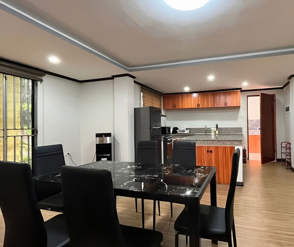 A modern kitchen with a central island, black chairs around a dining table, and wooden cabinets.
