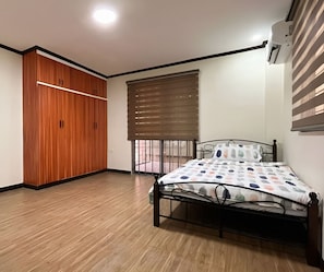 A bedroom with a bed, wooden wardrobe, and a window with blinds.