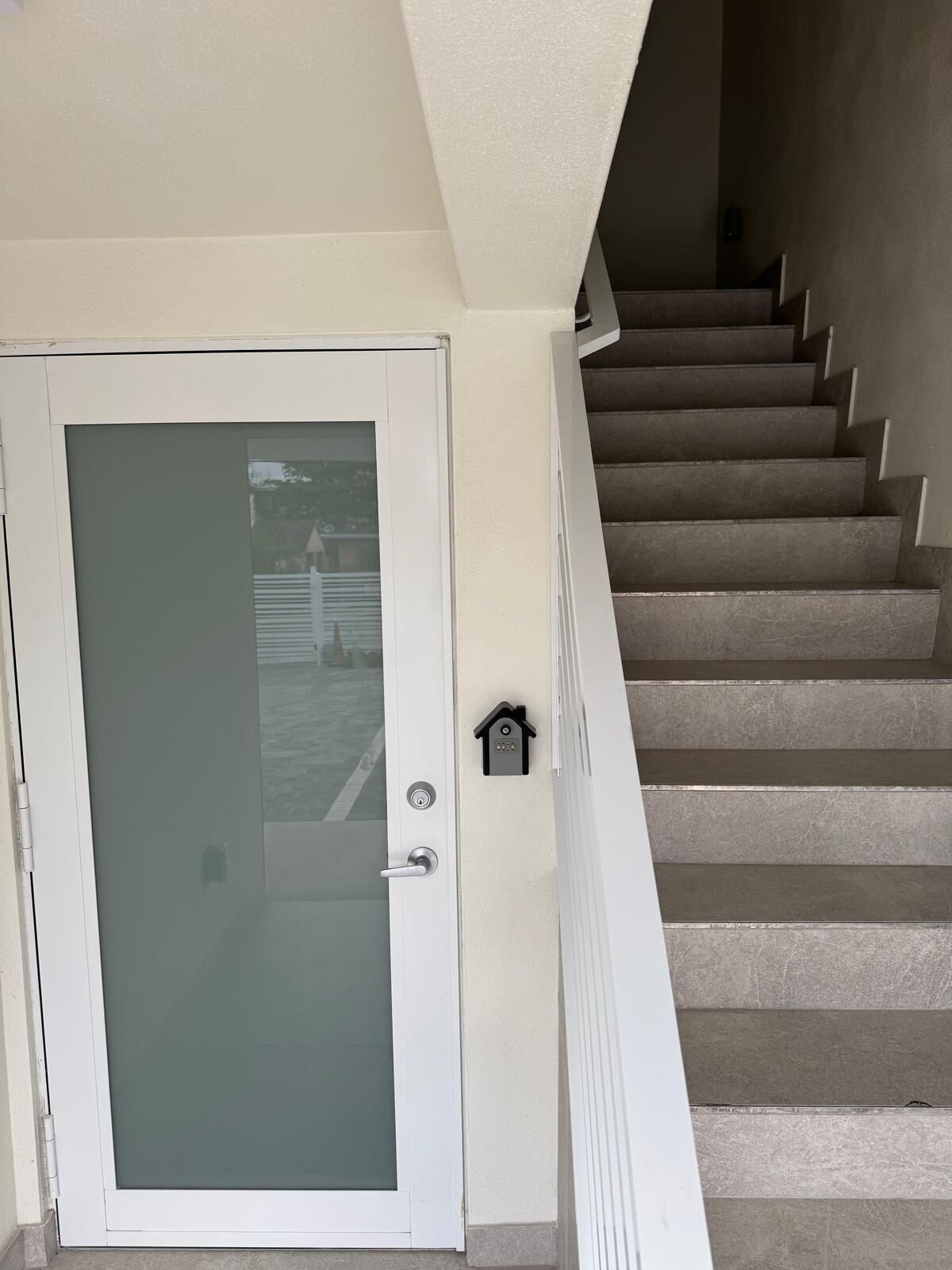 A white door with a frosted glass panel, a keyhole, and a small lock on the wall beside a staircase with beige steps.