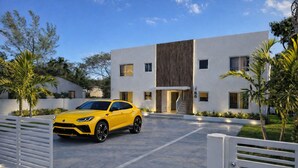 A modern building with a yellow car parked in front, a gated entrance, and a well-maintained lawn. - 
Charming 2BR Near Wynwood, Design District & Midtown (Miami)