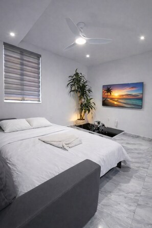 A modern bedroom with a bed, a ceiling fan, a potted plant, a painting, and a small sink.