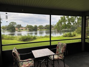 Ein Zimmer mit großem Fenster und Blick auf einen See, einem Tisch und zwei Stühlen.